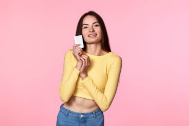 Sarı elbiseli genç, çekici bir kadın pembe arka planda plastik kredi kartı tutuyor.