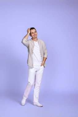 Pastel mor arka planda poz veren rahat gömlekli yakışıklı bir adam. Tam boy fotoğraf