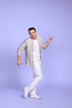 Pastel mor arka planda dans eden neşeli, genç, yakışıklı bir adam. Tatil yazı. Tüm vücut