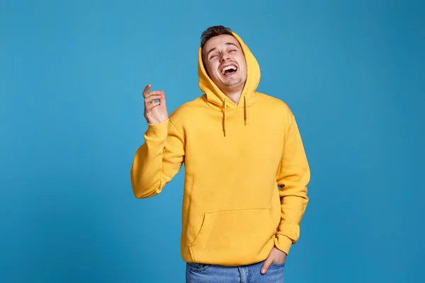 positive handsome man in yellow sweatshirt laughing on blue background