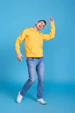 Mavi arka planda dans eden neşeli, genç ve yakışıklı bir adam. Tüm vücut