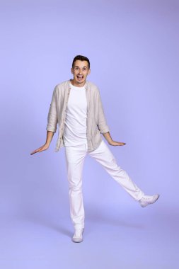 Pastel menekşe arka planda yalnız poz veren rahat gömlekli mutlu genç adam. Eğleniyoruz, takılıyoruz.