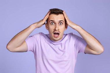 Şaşırmış bir adam, sürpriz bir ifadeyle, korku ve heyecan dolu bir yüz ile Pastel mor stüdyo arka planında
