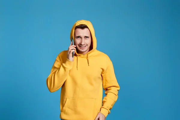 Upset angry man in yellow sweatshirt holding mobile phone and feel outraged isolated on blue background