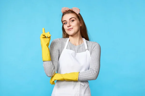 beautiful woman in rubber gloves and apron holding index finger up with new idea on blue background. cleaning