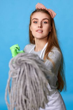 Lastik eldivenli genç kadın mavi arka plandaki kameraya paspası gösteriyor..