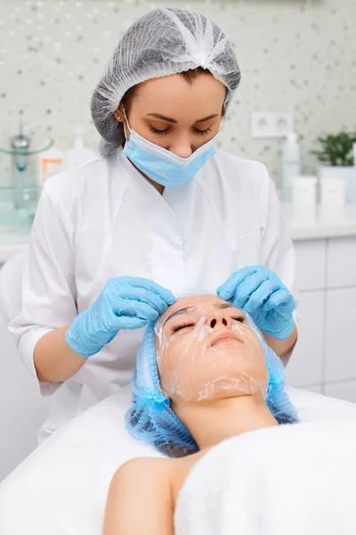 beautician applies hydrating sheet mask to the face of beautiful woman in the spa salon. spa treatments