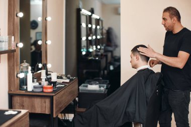 Barber and satisfied bearded man while sitting in chair at barbershop
