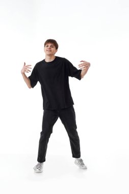 Beyaz arka planda dans eden siyah tişörtlü ve kot pantolonlu heyecanlı genç adam. Tam uzunluk