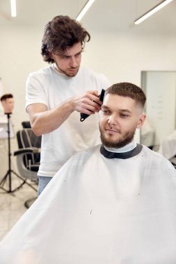 Berber dükkanındaki sakallı yakışıklının saçını kırpıcı ile kesiyor..