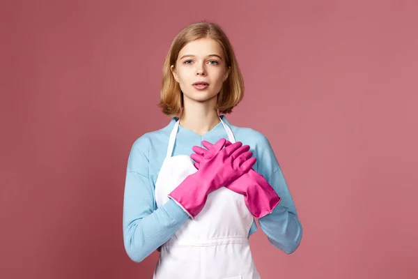 friendly grateful blonde woman in rubber gloves with hands on chest with closed eyes on pink background