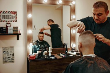 Dnipro, Ukraine, October 7, 2022: master hairdresser cutting his handsome happy young bearded caucasian guy.