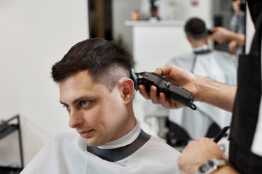 Barber trim hair with clipper on handsome man in barber shop.