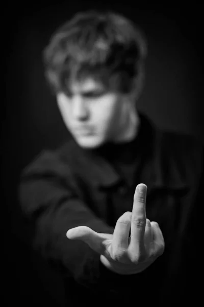 Young man showing middle finger doing fuck you gesture. black and white. focus on finger