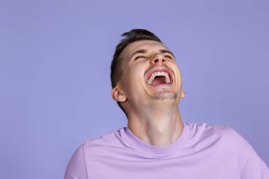 positive handsome man laughing on pastel purple studio background