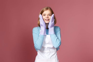 surprised young blonde woman in rubber gloves and cleaner apron on pink background.