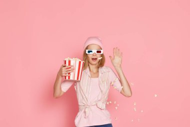 Kısa saçlı, korku filmi izleyen, elinde pembe arka planda bir kova patlamış mısır tutan korkmuş bir kız.