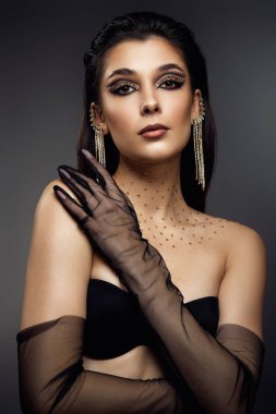 Gri arka planda uzun küpeli, okları ve yapay elmasları olan, yaratıcı göz makyajlı, güzel, modaya uygun bir kadın.