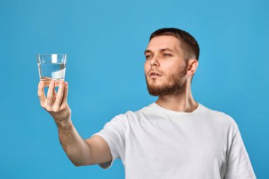 handsome bearded man with drinking glass of water smiling happy on blue background. focus on glass