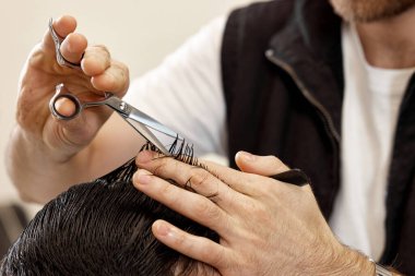 close-up, professional hairstylist does haircut for caucasian client man at barber shop.