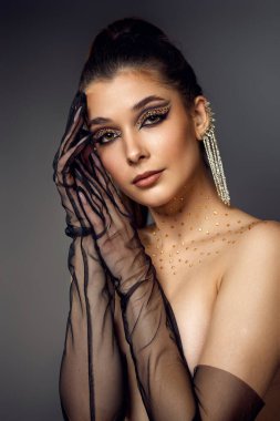 Gri arka planda uzun küpeli, okları ve yapay elmasları olan, yaratıcı göz makyajlı, güzel, modaya uygun bir kadın.