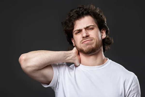 young man with neck pain due to stress on dark gray background