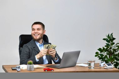 young bearded businessman working on laptop and counting dollars money at office desk