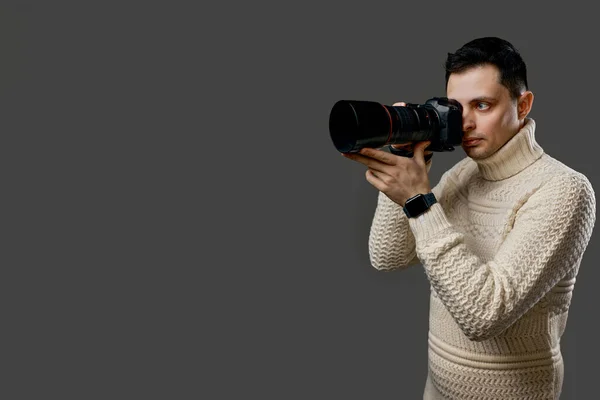 Professional young handsome photographer in sweater with digital camera isolated on gray background. copy space for text