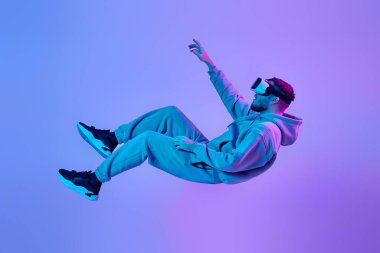 young man using virtual reality glasses levitating in the air on blue background. Neon lighting