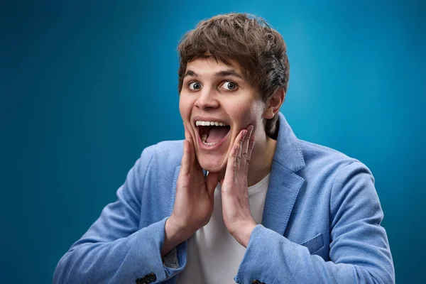 happy shocked man with surprise expression and excited face on blue studio background