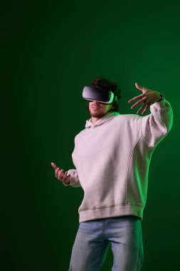 man in sweatshirt using virtual reality headset on green background. Neon lighting