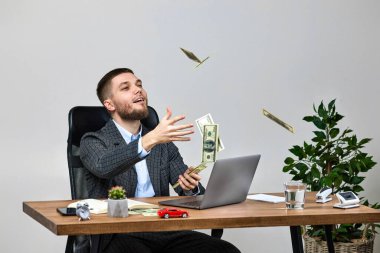 young bearded businessman working on laptop and throwing dollar bills in the air