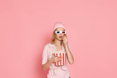 Kısa saçlı, korku filmi izleyen, elinde pembe arka planda bir kova patlamış mısır tutan korkmuş bir kız.