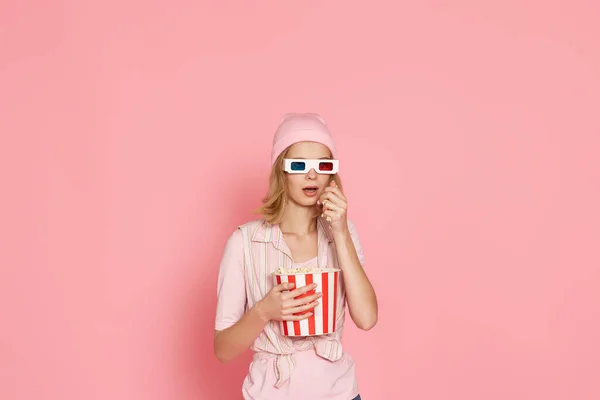 terrified girl with short haircut watching horror movie , holding bucket of popcorn on pink background