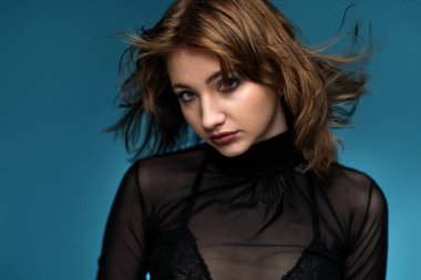 young woman with stylish hairstyle posing in black leather jacket on blue background.