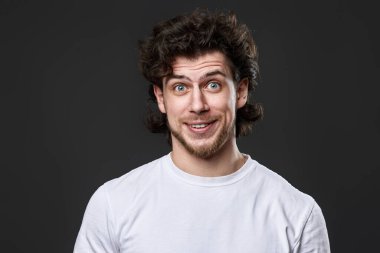 portrait of young smiling curly man in white t-shirt on dark gray background
