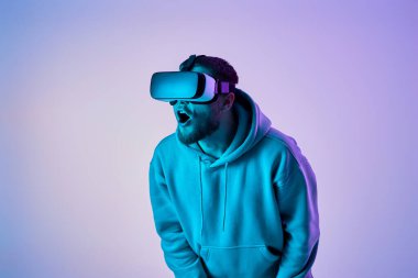 Astonished man using virtual reality glasses and playing video games on blue background. Neon lighting