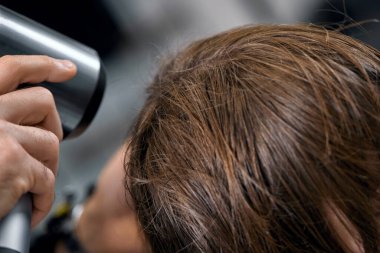 man hairdresser dries female hair with hairdryer after washing in the beauty salon.