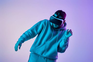 man in sweatshirt using virtual reality glasses and playing video games on blue background. Neon lighting