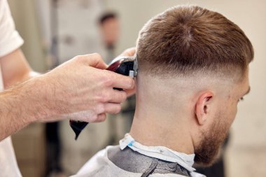 Berber dükkanındaki sakallı yakışıklının saçını kırpıcı ile kesiyor..