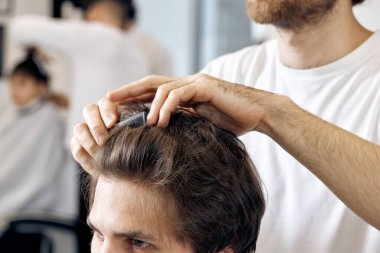 close-up, professional male hairstylist combing young customers hair in barbershop