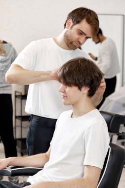 Barber combing caucasian man while sitting in chair before haircut at barbershop. client tells what haircut he wants