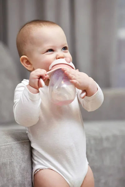 快乐的小女孩在家里拿着瓶子和饮用水 — 图库照片