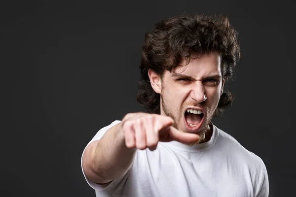furious caucasian man pointing finger at you and the camera on dark gray background