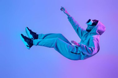 young man using virtual reality glasses levitating in the air on blue background. Neon lighting