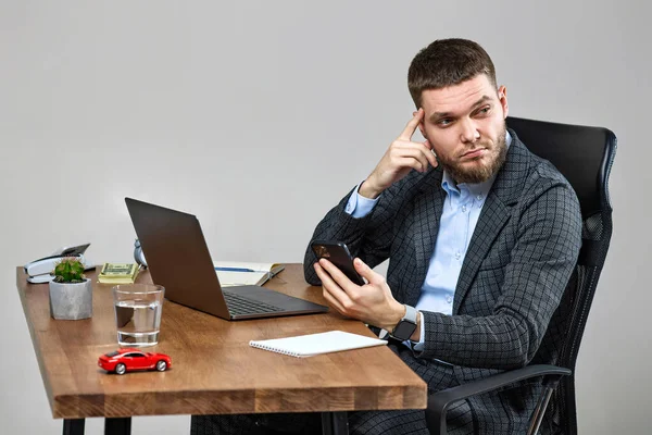 Young Bearded Businessman Sitting Chair Desk Holding Phone Using Laptop — Stok fotoğraf