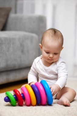 Evdeki halının üzerinde renkli oyuncak piramidiyle oynayan tatlı bir bebek. Çocuklar için erken gelişme.