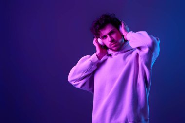 handsome man listening to music with wireless headphones on blue background. Neon lighting