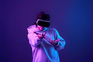 man in sweatshirt using virtual reality glasses on blue background. Neon lighting