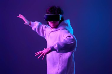 Gözlüklü ve kazaklı bir adam mavi arka plandaki bir şeye dokunmaya çalışıyor. Neon ışıkları